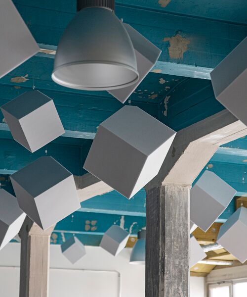 Raum mit blauer Decke, von der graue Würfel-Objekte und Lampen künstlerisch herabhängen.