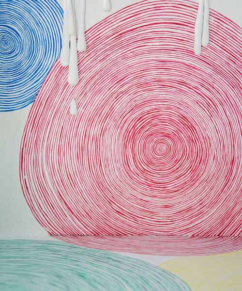 Bunte Kunstinstallation mit spiralförmigen Linien in Blau, Rot, Grün und Gelb auf einer weißen Fläche, von der weiße Wachstropfen herablaufen.