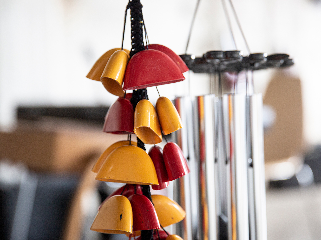 Bunte Klangglocken in Rot und Gelb hängen an schwarzen Schnüren, im Hintergrund sind silberne Klangröhren zu sehen.