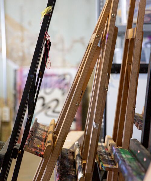 Mehrere Staffeleien mit Farbresten in einem Kunstatelier, im Hintergrund unscharfe Wände mit kreativen Spuren.